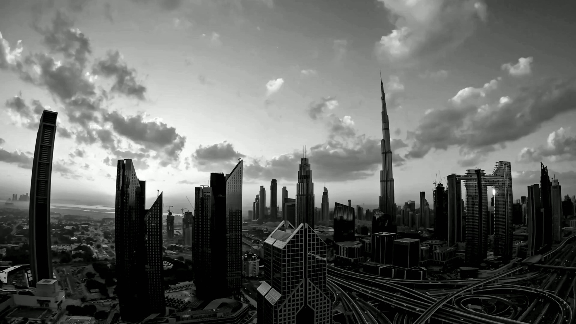 Institutional commercial property investment advisory at Mitchell's — the Sheikh Zayed Road tower corridor and its interchange in black and white, the Burj Khalifa among the skyline
